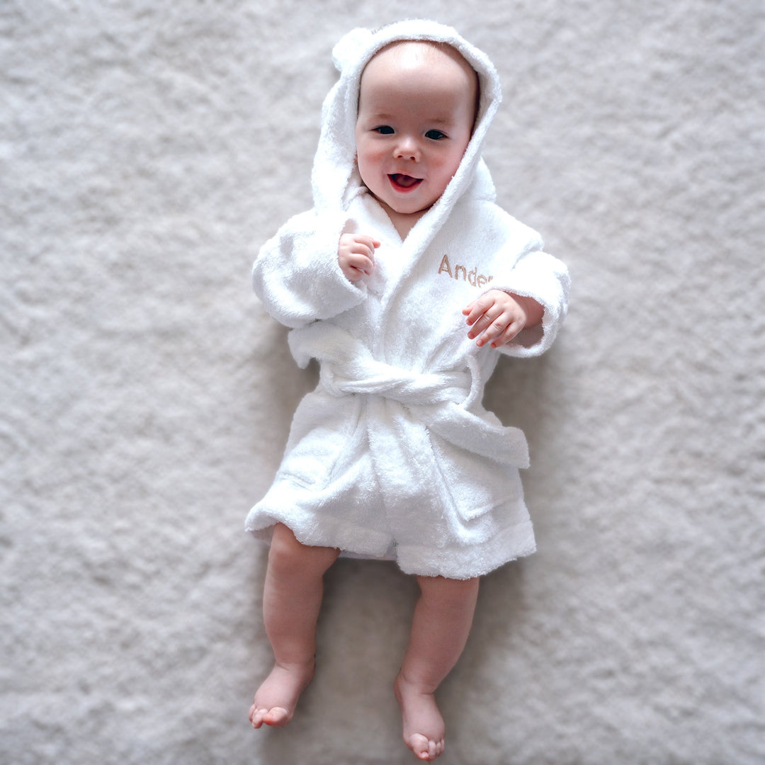 Baby in white bamboo robe with "Ander" customised in beige thread