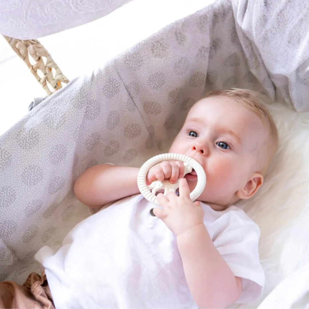 Baby holding a Sophie la Girafe Circle teething ring in a crib with soft bedding