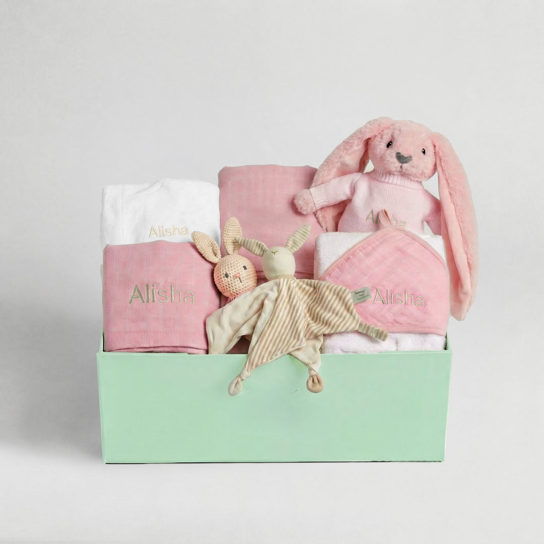 Baby gift set with pink and white items, including a bunny plush toy, on a light gray background.