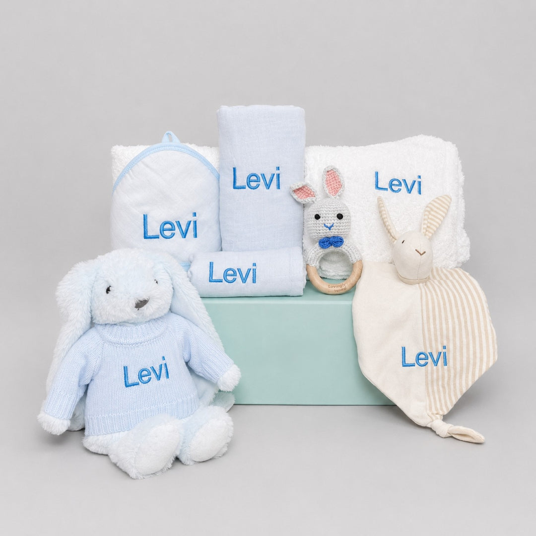 Collection of baby items including a plush bunny, blanket, and toys in a 'Yoyo' branded box on a light gray background.