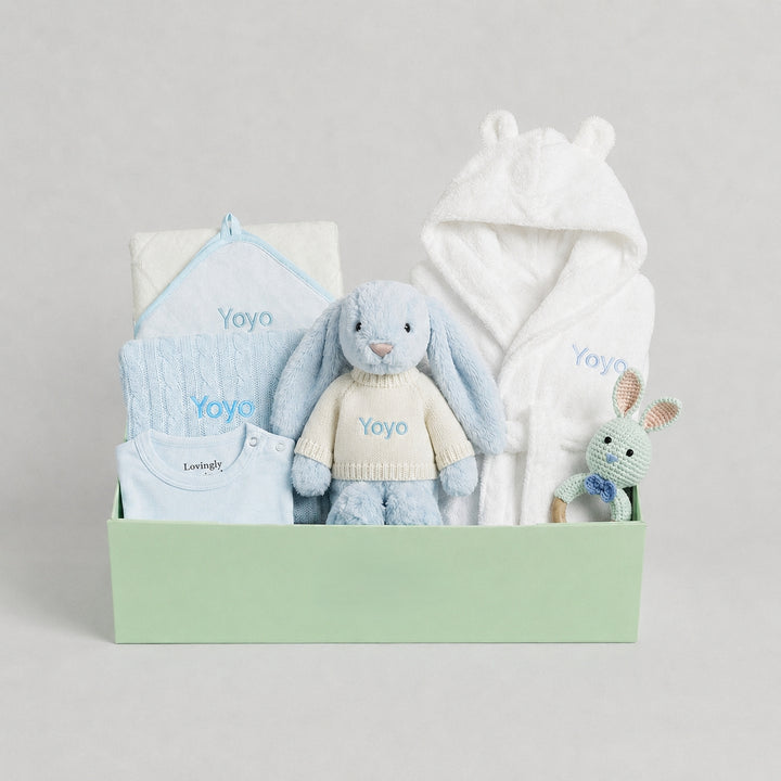Baby gift set with plush toys, clothing, and a blanket in a box on a light gray background.
