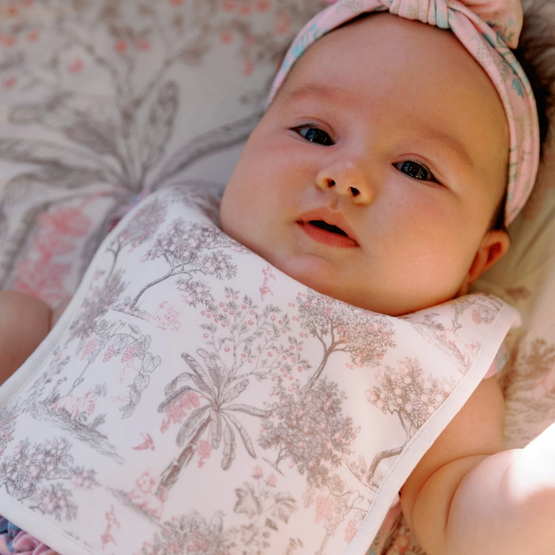 Baby wearing the House of Holly Fruit Toile reversible bamboo drool bib in pink, styled with a matching floral headband.