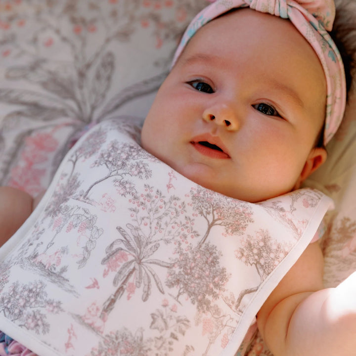 Baby wearing the House of Holly Fruit Toile reversible bamboo drool bib in pink, styled with a matching floral headband.
