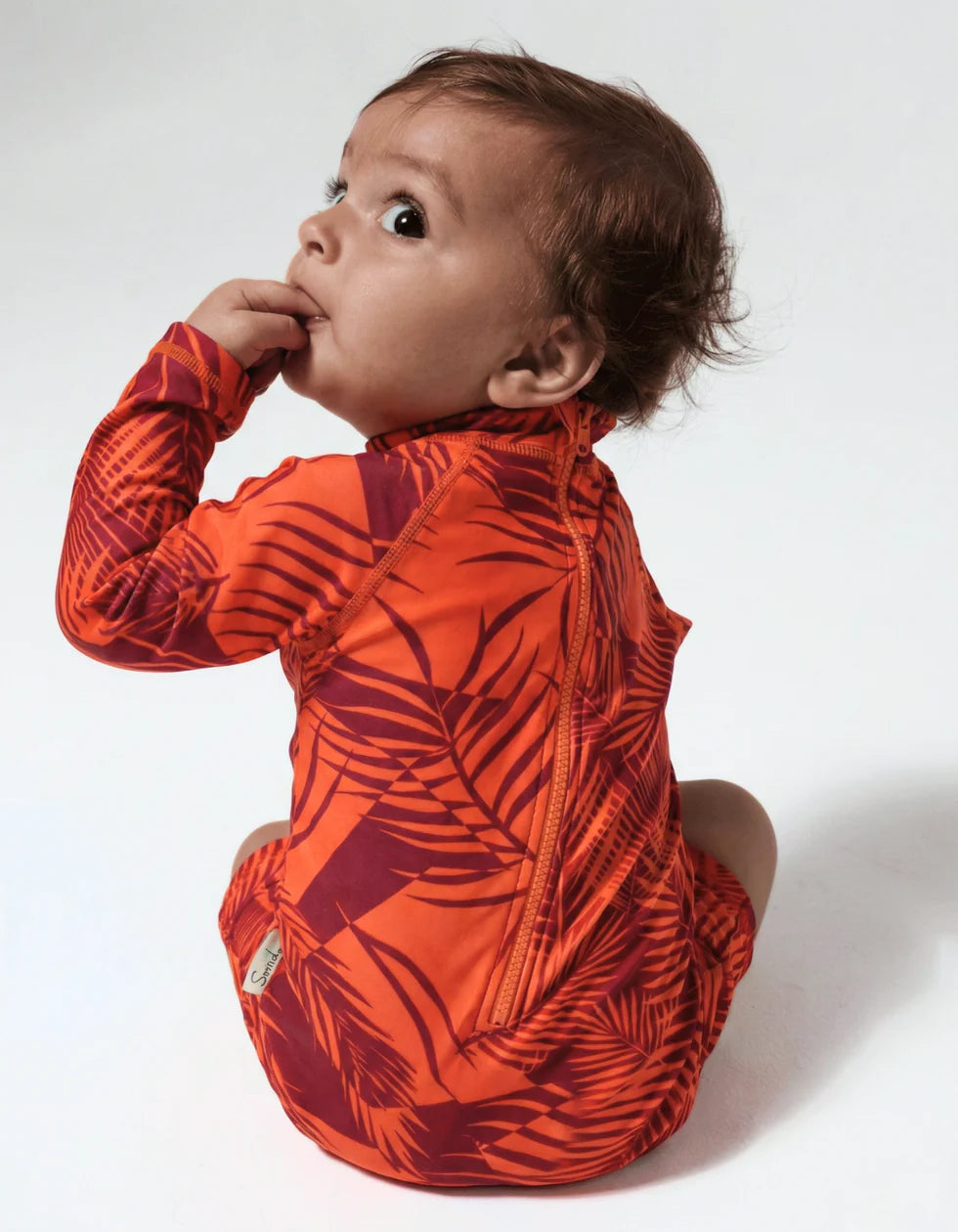 Back view of a Baby girl wearing an orange patterned swimsuit on a white background