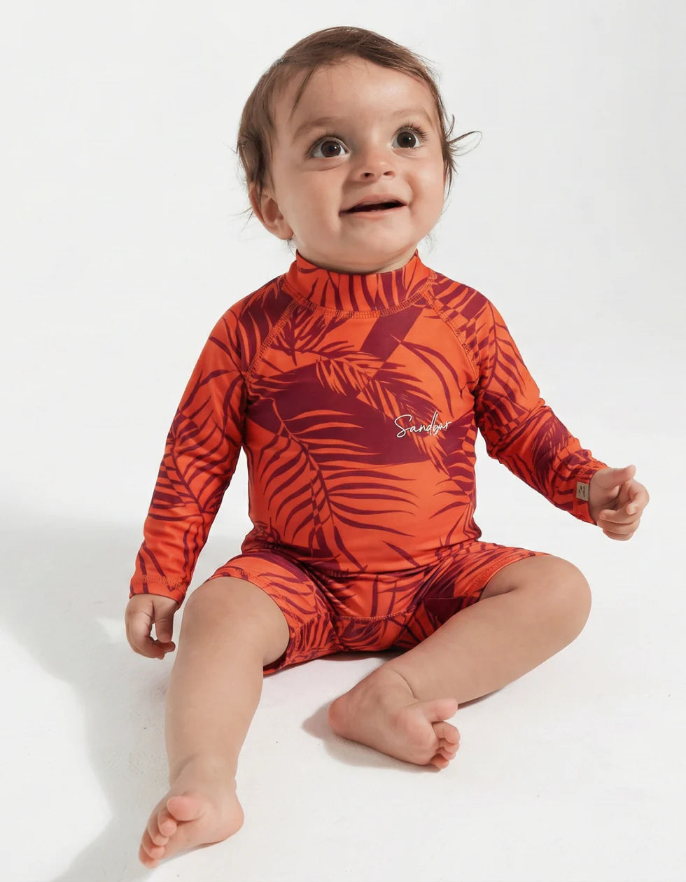 Baby wearing an orange leaf-patterned swimsuit on a white background