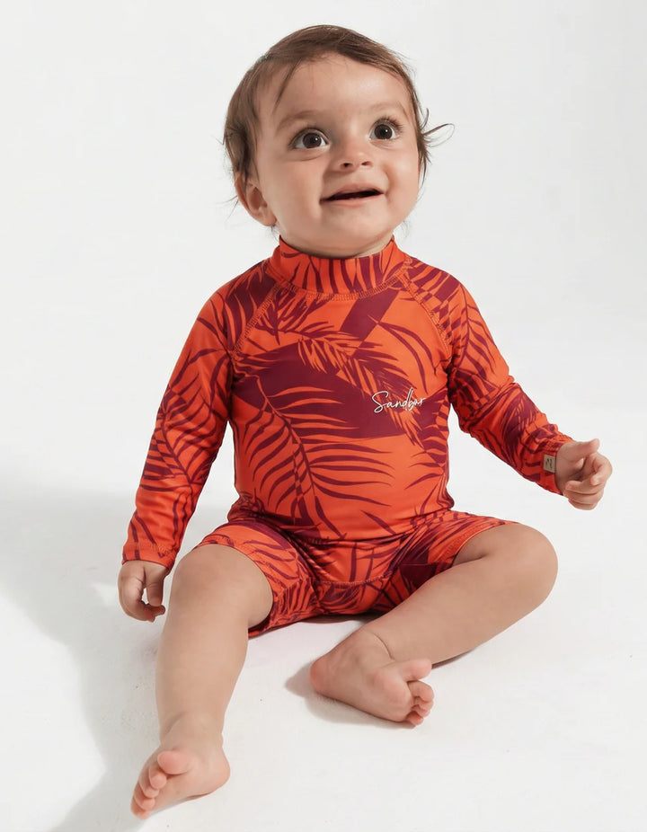 Baby wearing an orange leaf-patterned swimsuit on a white background