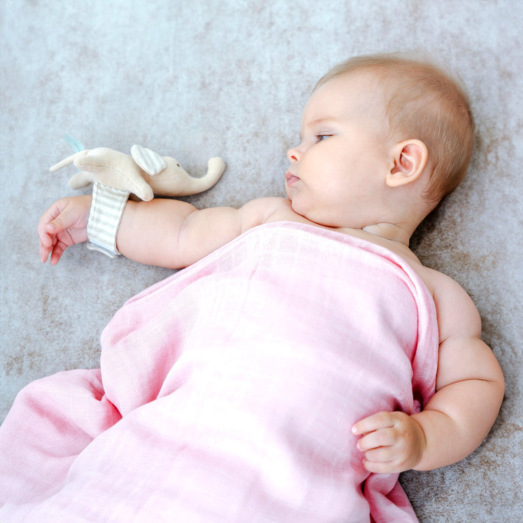 Baby covering with Pink Bamboo Swaddle and wearing elephant wrist rattle
