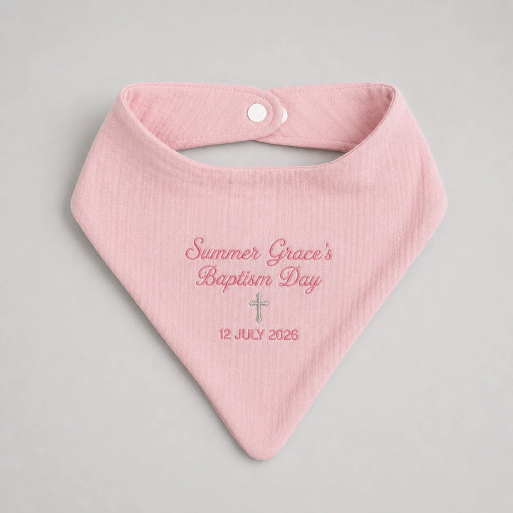 A light pink muslin baby bib with custom embroidered text reading 'Summer Grace's Baptism Day' and a date '12 JULY 2026' on a neutral gray background.
