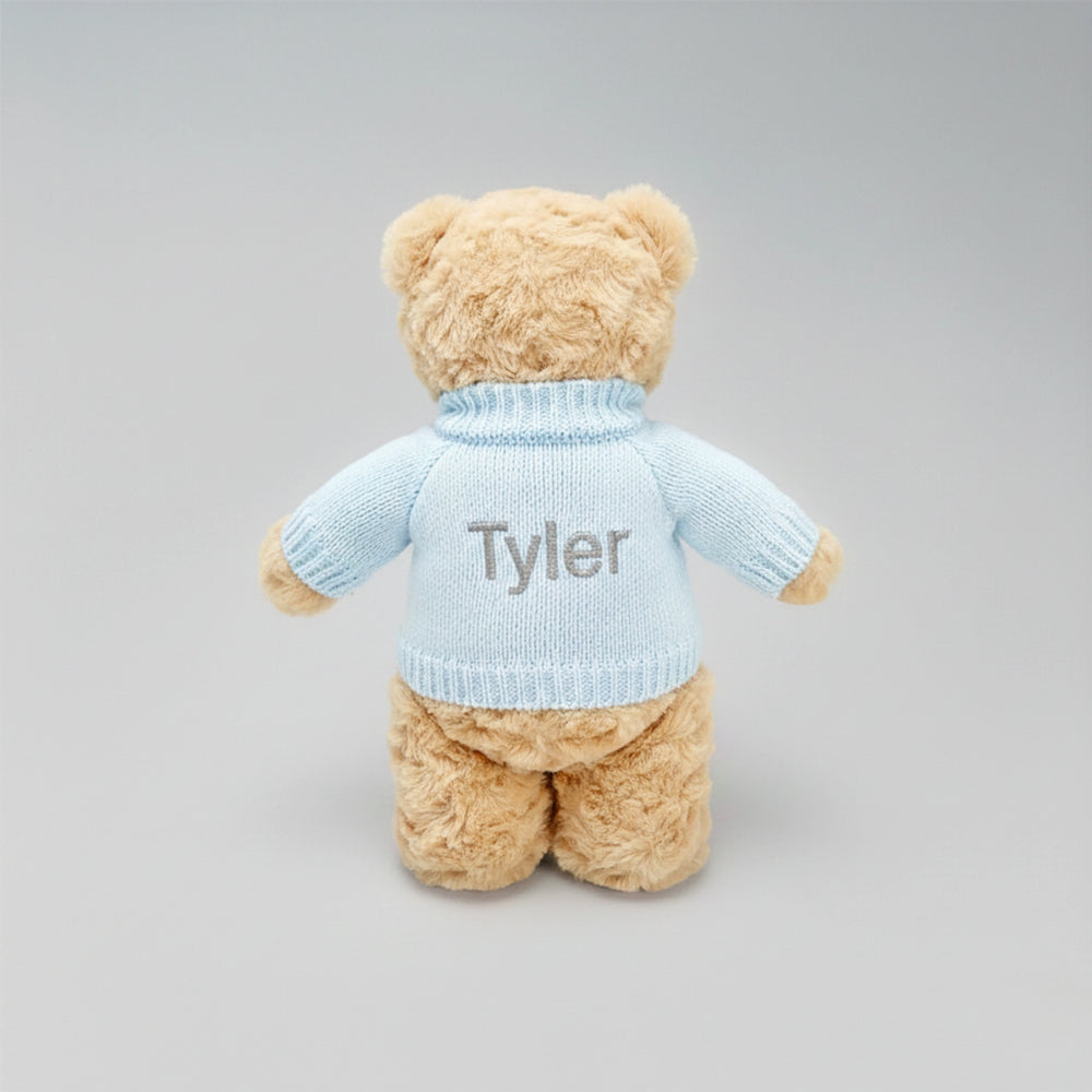 Teddy bear wearing a light blue sweater with 'Tyler' embroidered on it against a gray background