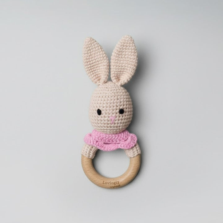 Crocheted bunny rattle with wooden ring on a light gray background