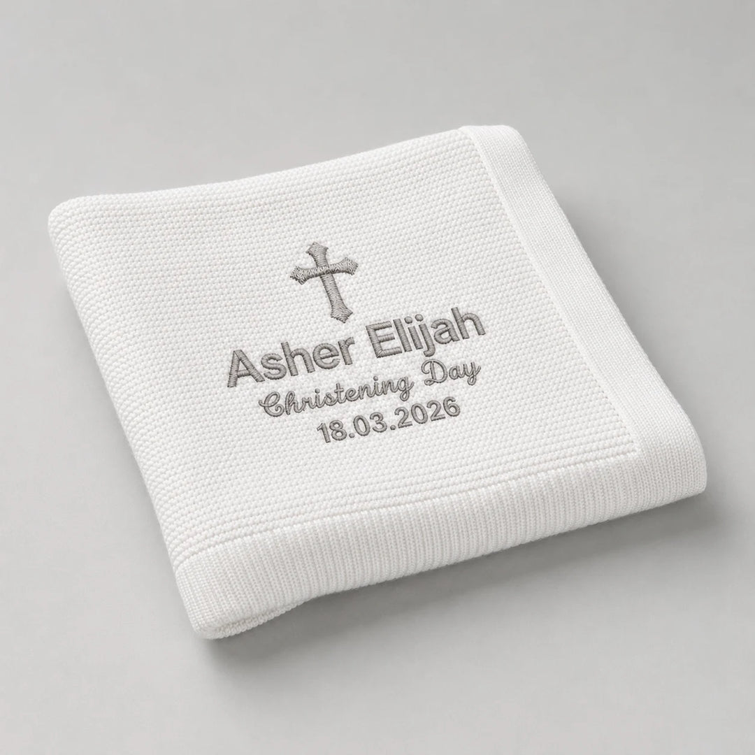 White embroidered blanket with cross and text on a gray background