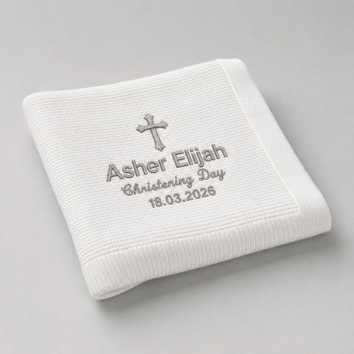 White embroidered blanket with cross and text on a gray background