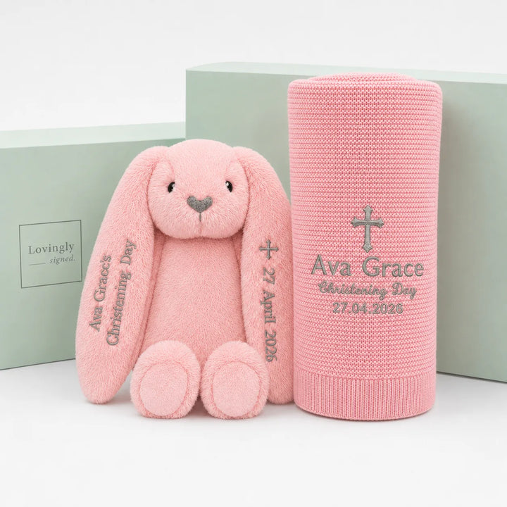 A pink plush bunny and matching pink knitted keepsake blanket set, both personalised with the name 'Ava Grace' and a date, displayed in front of a mint green gift box on a white background.