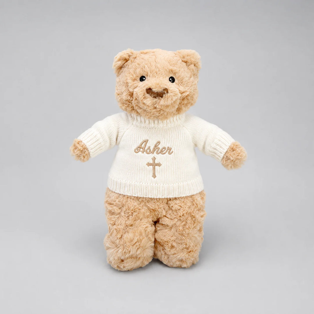 A plush teddy bear wearing a cream-colored knit sweater with the name 'Asher' and a cross embroidered on the front, set against a solid gray background.