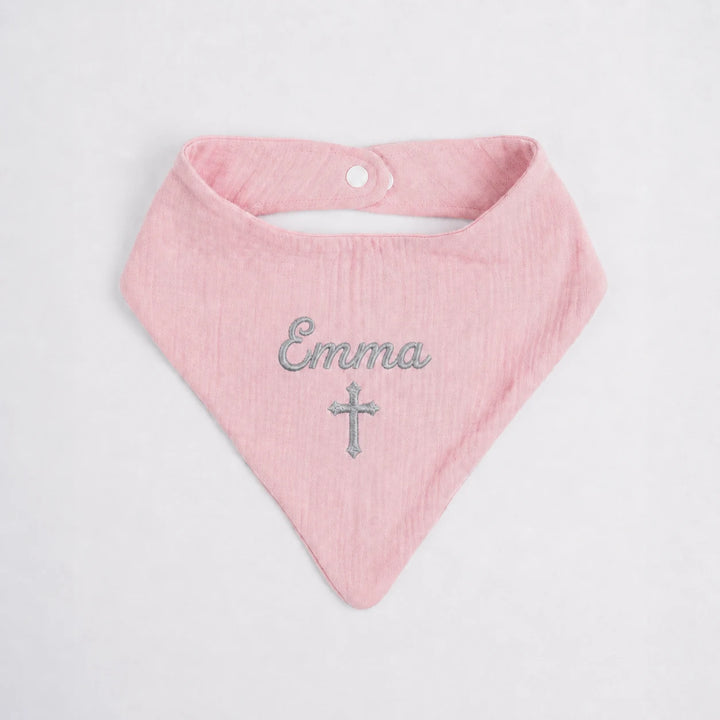 A light pink cotton bandana bib with 'Emma' and a cross embroidered in gray on the front, displayed flat against a white background.