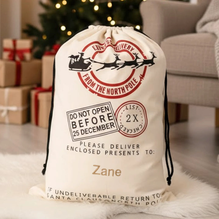 Christmas gift sack with Santa Claus stamp design, placed on a carpeted floor with Christmas decorations in the background.