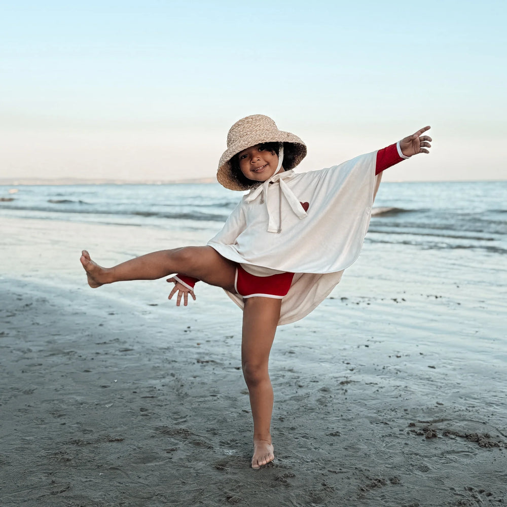 Kid by the beach wearing Cosy Roots Organic UV Poncho - Sand