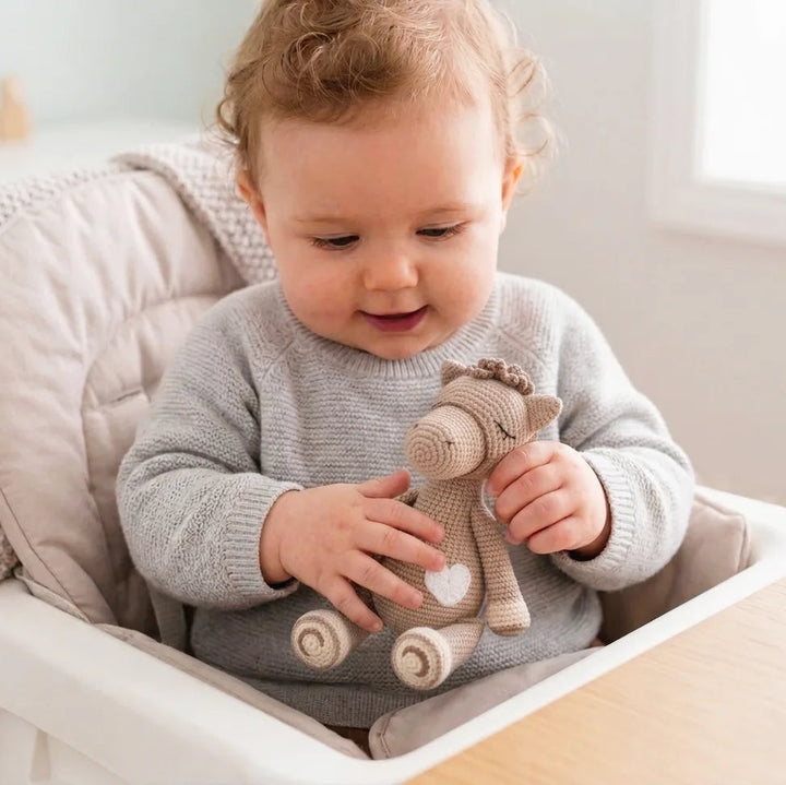 Baby Playing with Hand-Crocheted Horse Rattle Toy in a High Chair