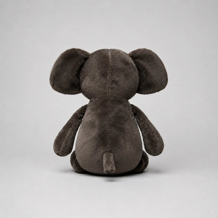 Back view of a grey elephant soft toy with oversized ears, floppy arms and a small tail, photographed on a light grey studio background.