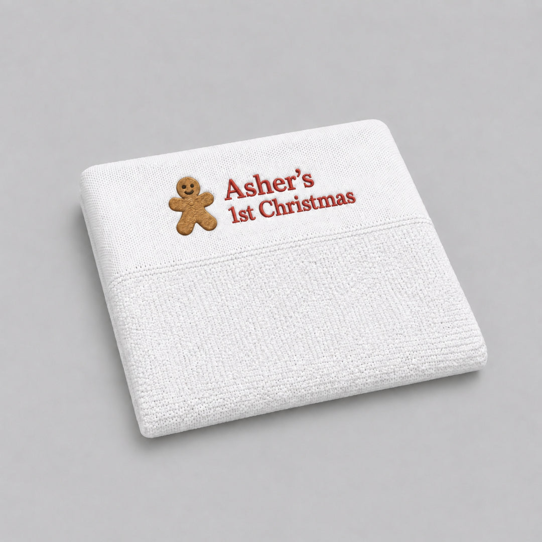 White personalised knitted Christmas baby blanket embroidered with a gingerbread man and “Asher’s 1st Christmas” in red, photographed on a light grey studio background.