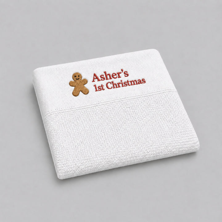  White personalised knitted Christmas baby blanket embroidered with a gingerbread man and “Asher’s 1st Christmas” in red, photographed on a light grey studio background.