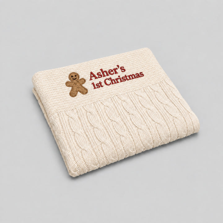 Cream cable-knit baby blanket personalised with a gingerbread man motif and “Asher’s 1st Christmas” embroidered in red.