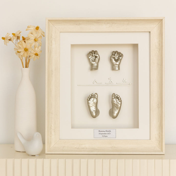 Framed metallic hand and footprints on a decorative shelf with a vase and flowers.