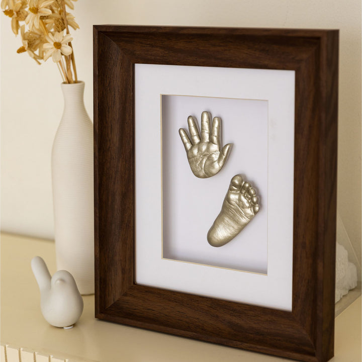 Framed metallic baby hand and footprints on a white background with decorative elements.