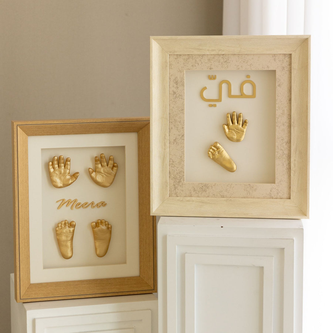 Two gold-framed wall art pieces with hand and footprints on a neutral background.