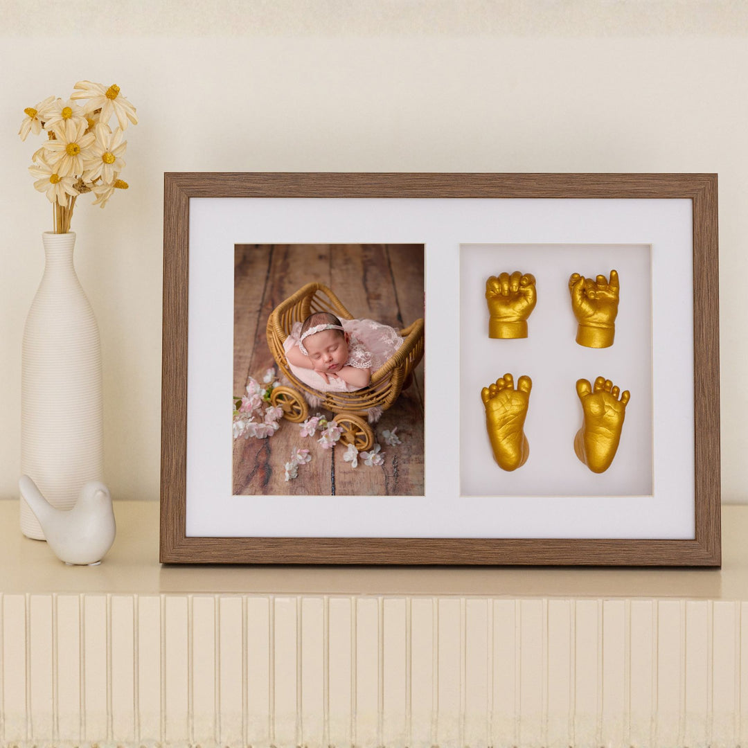 Framed photo of a baby in a basket with gold baby fist and foot casts on a shelf.
