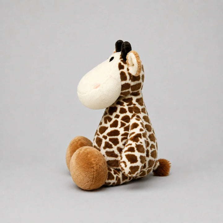 Side view of a brown and cream giraffe soft toy with a cream face, black horns and oversized feet, photographed on a light grey studio background.
