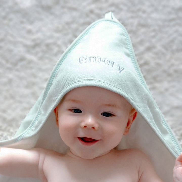 Baby in Green Hooded towel with name "Emery" embroidered in grey thread