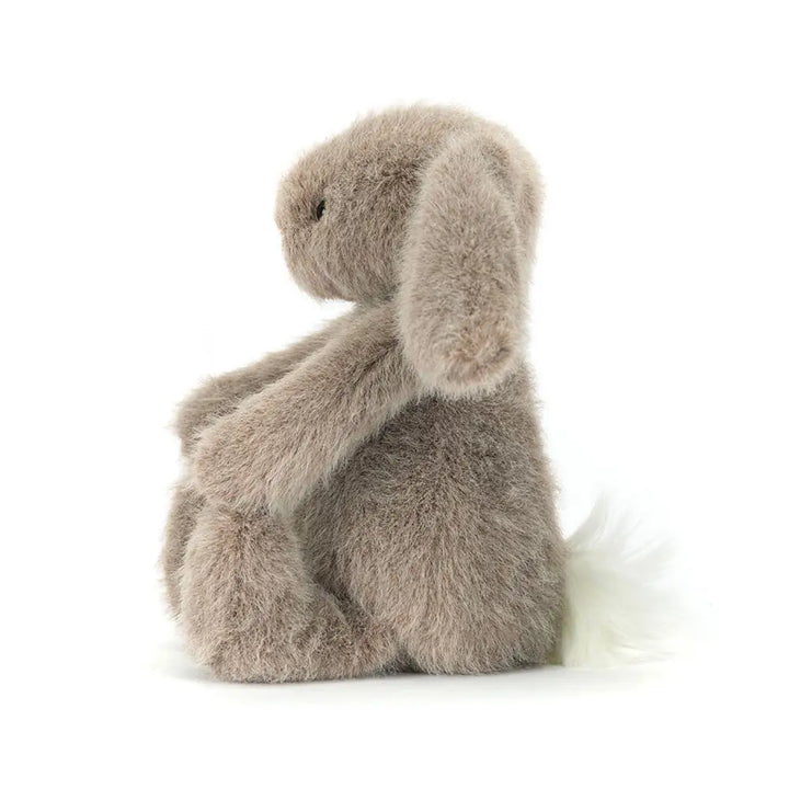 Side profile of Jellycat Fawn Flufflet Bunny showing its long floppy ear, rounded body, soft taupe fur and fluffy white tail.