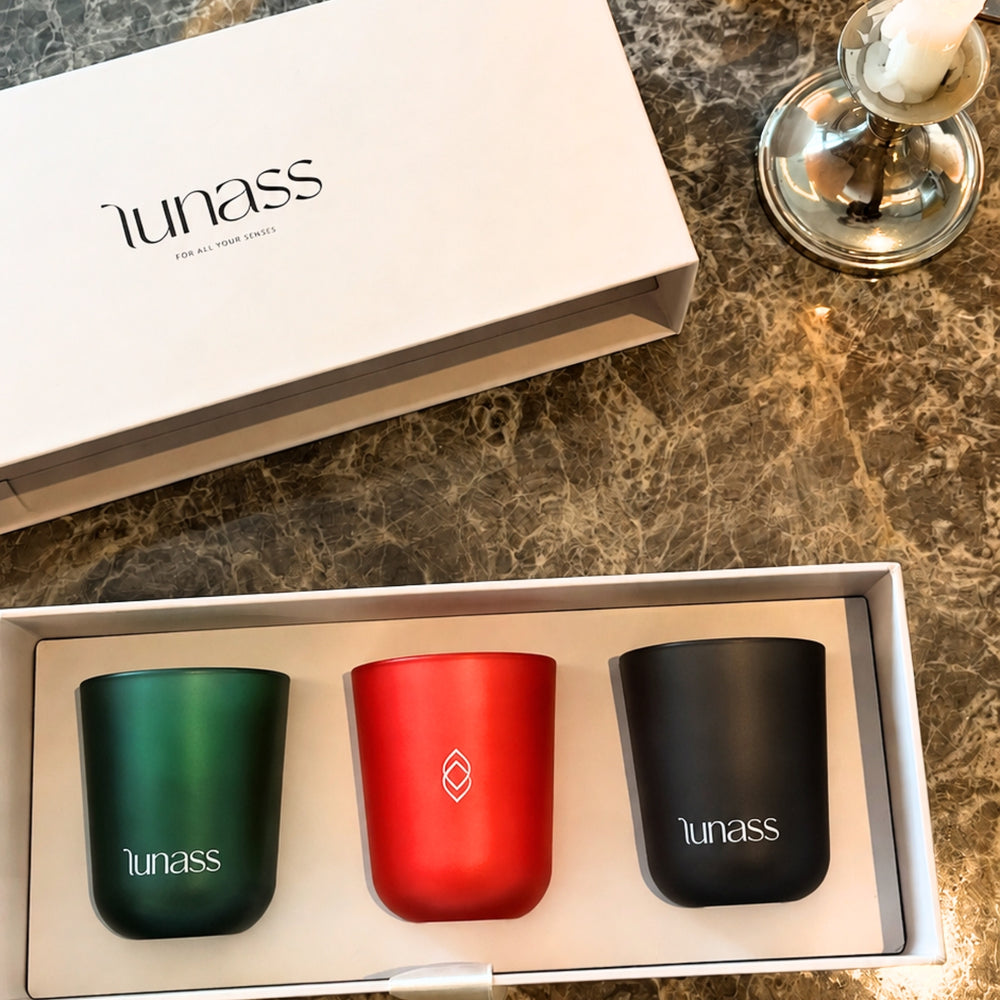 LUNASS luxury candle gift set featuring green, red and black scented candles arranged in a white presentation box on a marble surface with warm candlelight.