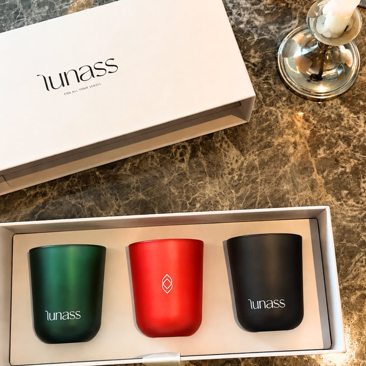 LUNASS luxury candle gift set featuring green, red and black scented candles arranged in a white presentation box on a marble surface with warm candlelight.