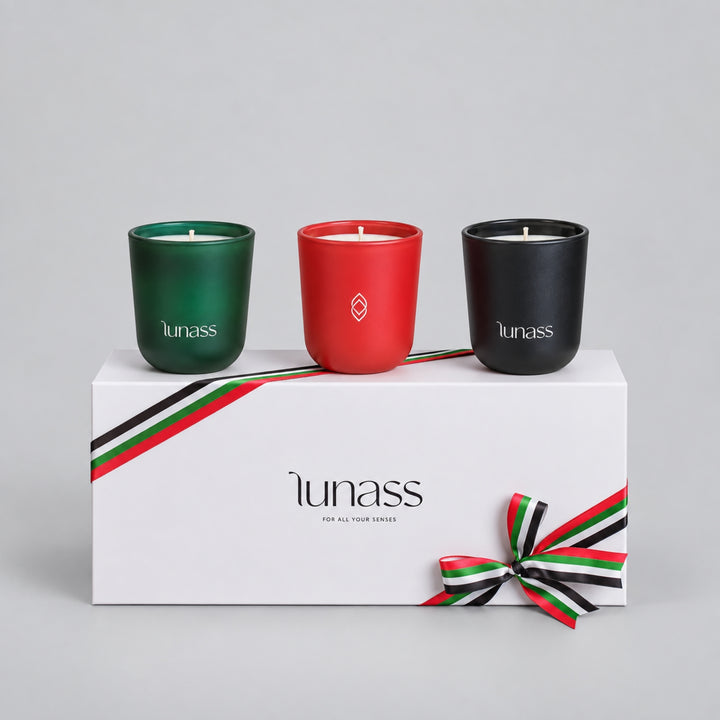 LUNASS trio candle gift set with green, red and black candles displayed above a white presentation box with coordinated ribbon detail on a light grey studio background.