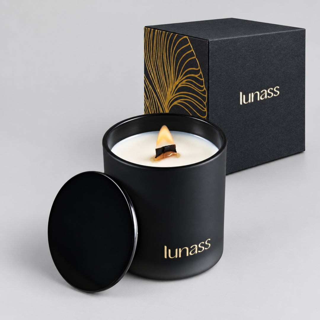 Lit black LUNASS scented candle with matching black and gold gift box and removable lid on a light grey studio background.