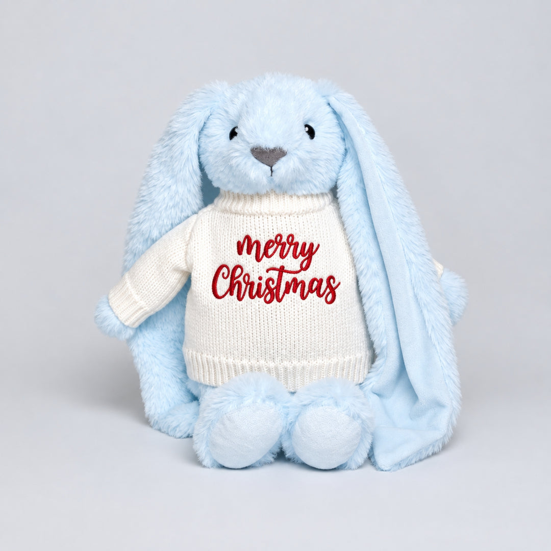 Blue bunny soft toy wearing a cream knitted jumper embroidered with “Merry Christmas” in red, photographed on a light grey studio background.