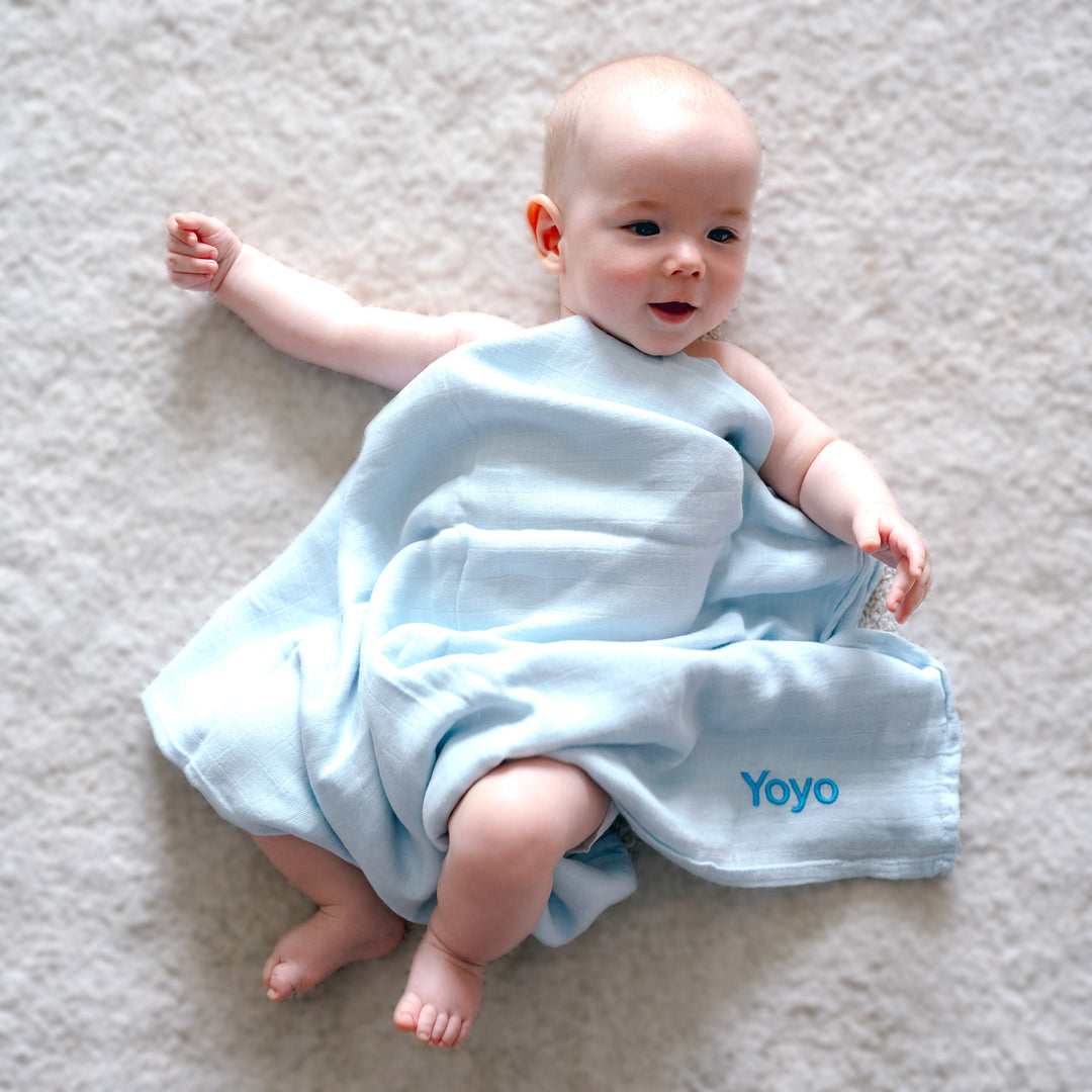 Baby covered with Blue Bamboo Muslin Swaddle with "Yoyo" personalised in Blue Thread
