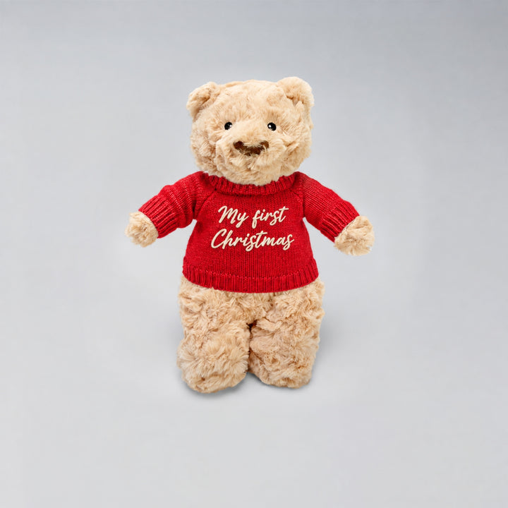 Christmas teddy bear wearing a red knitted jumper embroidered with “My First Christmas”, photographed on a light grey studio background.