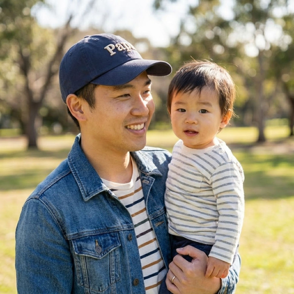 Man wearing a cap with 'Papa' holding a child in a park