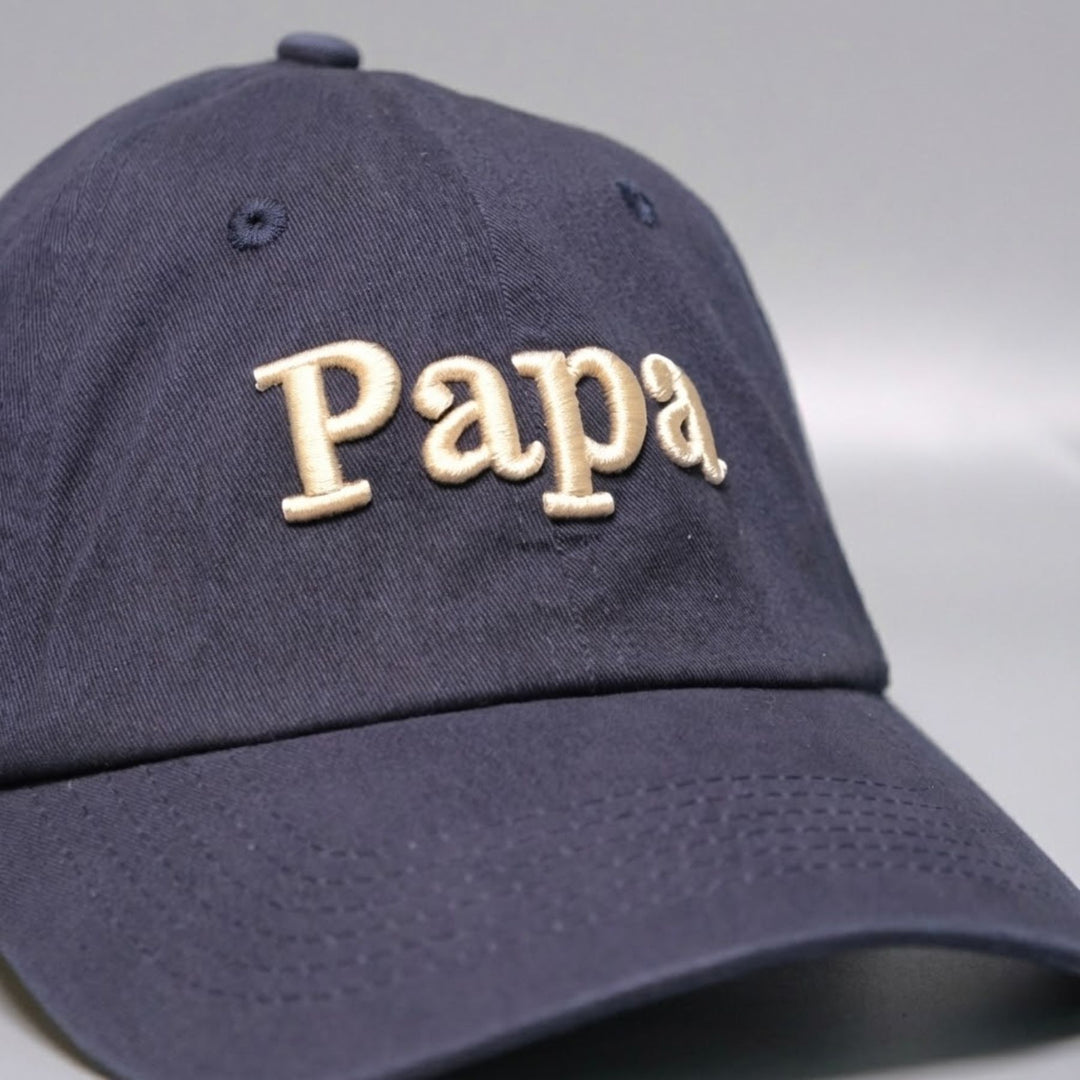 Navy blue cap with 'Papa' embroidered in beige on a gray background