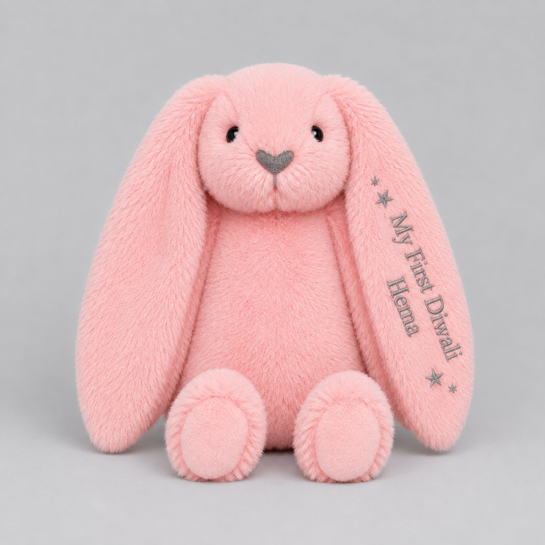 Personalised pink bunny soft toy embroidered with “My First Diwali Hema” and star details on the ear, photographed on a light grey studio background.