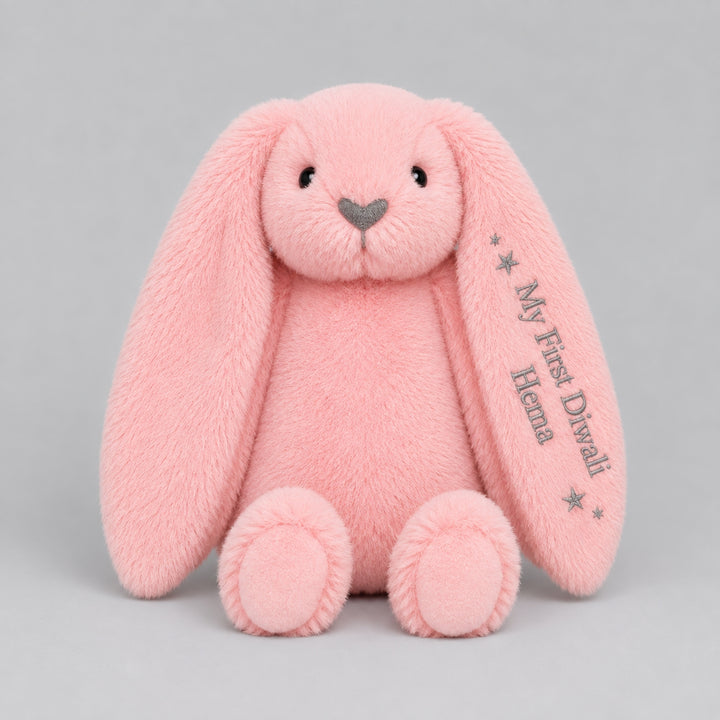 Personalised pink bunny soft toy embroidered with “My First Diwali Hema” and star details on the ear, photographed on a light grey studio background.