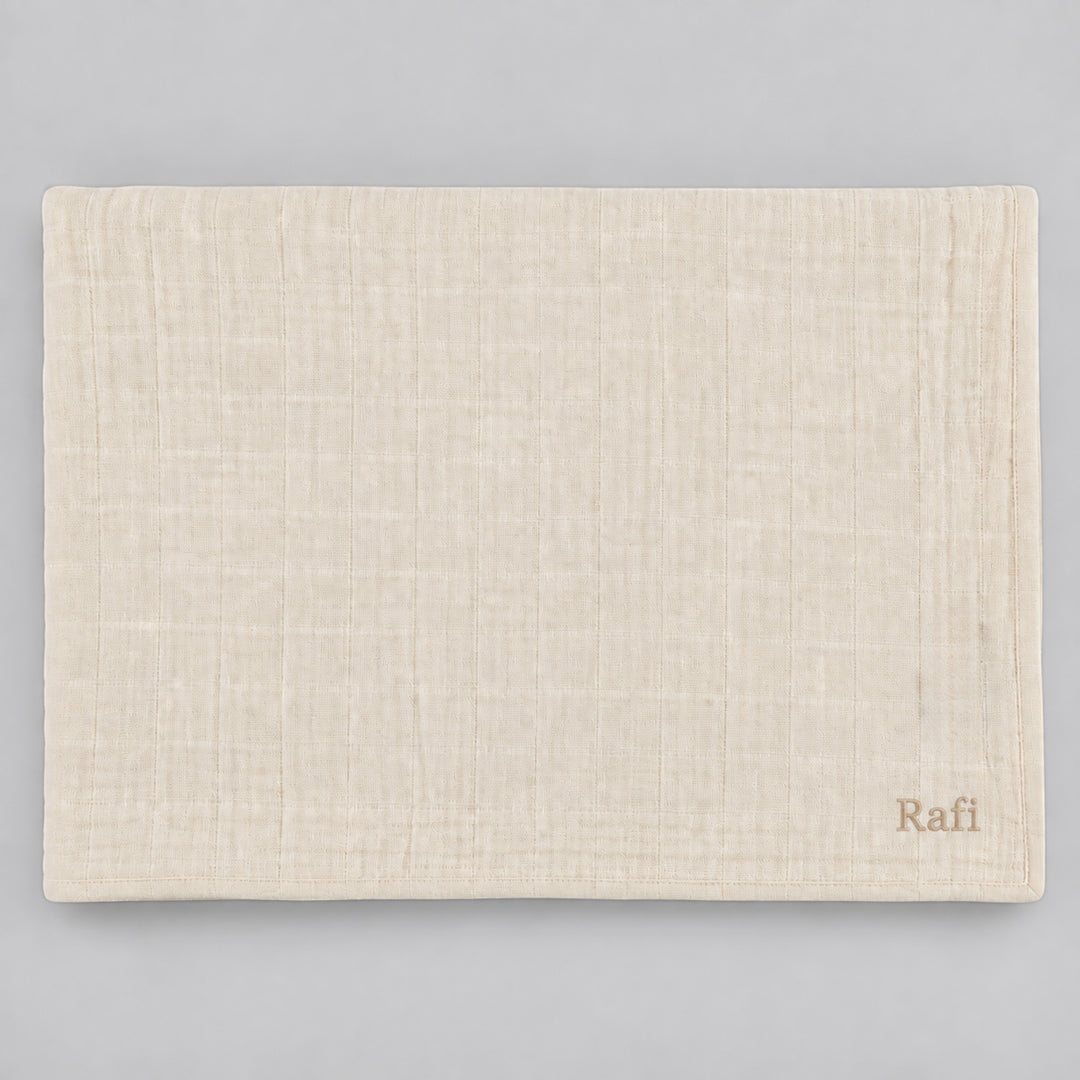 Beige Trixie muslin blanket displayed flat on a light grey studio background, personalised with the name “Rafi” embroidered in beige at the bottom right corner.