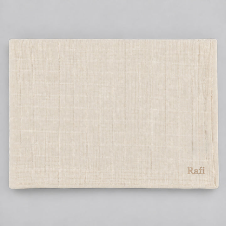 Beige Trixie muslin blanket displayed flat on a light grey studio background, personalised with the name “Rafi” embroidered in beige at the bottom right corner.