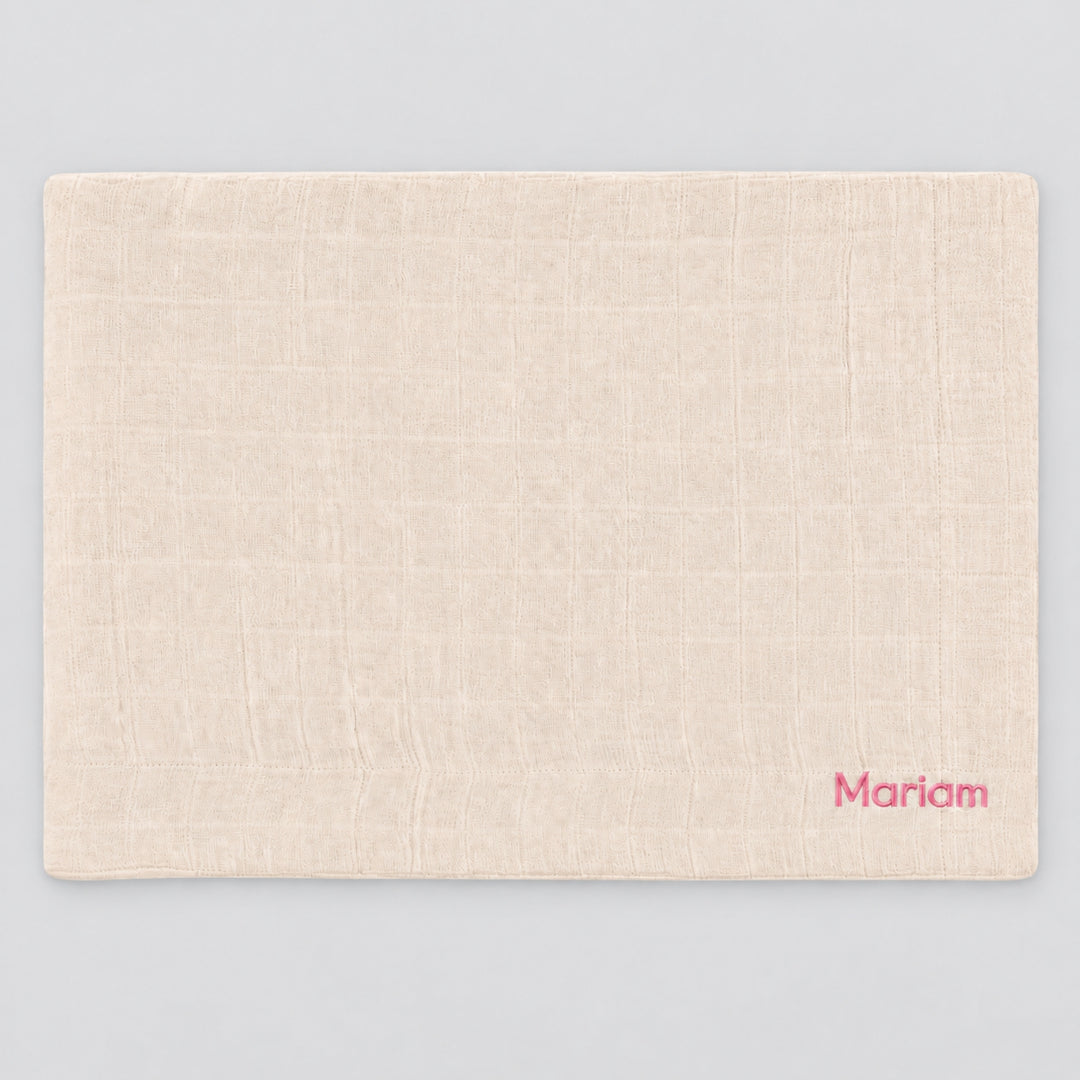Blossom Trixie muslin blanket laid flat on a light grey studio background, personalised with the name “Mariam” embroidered in pink at the bottom right corner.