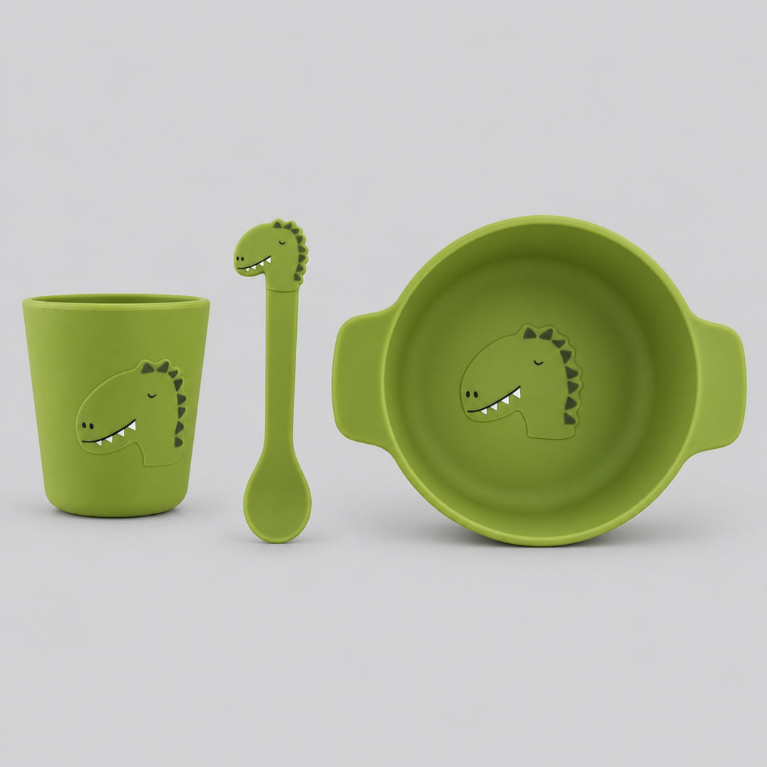Green Trixie dinosaur silicone mealtime set with handled bowl, cup and matching spoon on a light grey studio background.