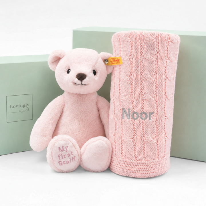 Personalised pink My First Steiff teddy bear with pink cable knit blanket embroidered “Noor,” displayed with Lovingly Signed gift boxes.