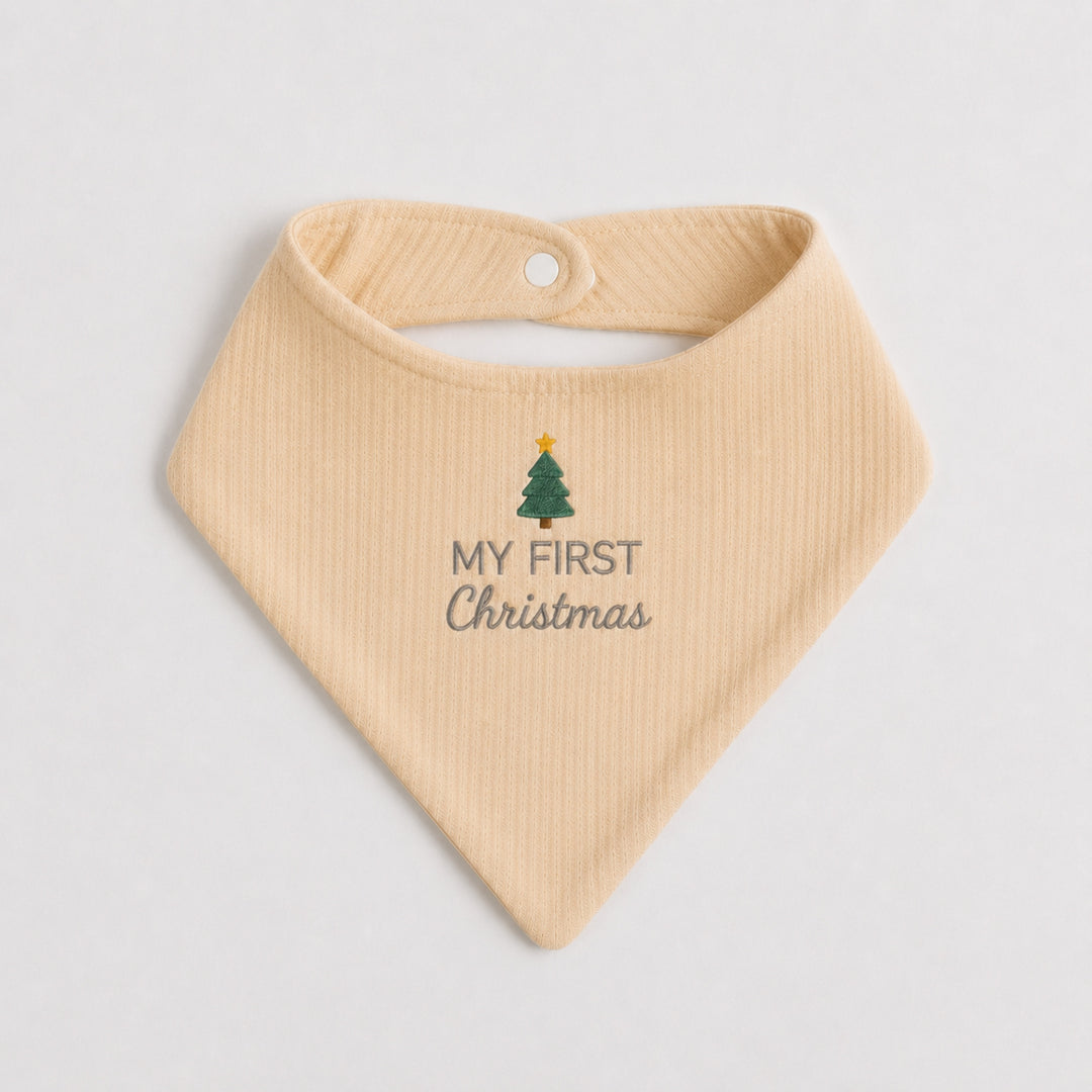 Cream baby bib embroidered with a green Christmas tree topped with a gold star and the words “My First Christmas” in grey, photographed on a clean white background.